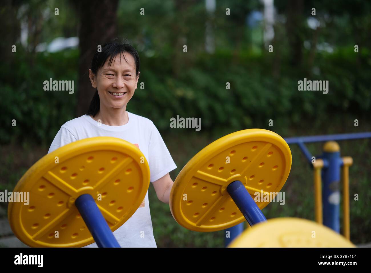 Una vecchia donna asiatica felice fa esercizio su attrezzature fitness all'aperto. Guardando la telecamera Foto Stock