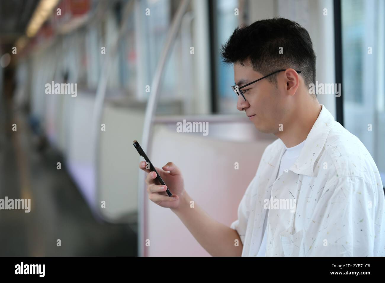 Giovane asiatico che usa lo smartphone all'interno della metropolitana. Il passeggero cinese guarda il telefono in metropolitana Foto Stock