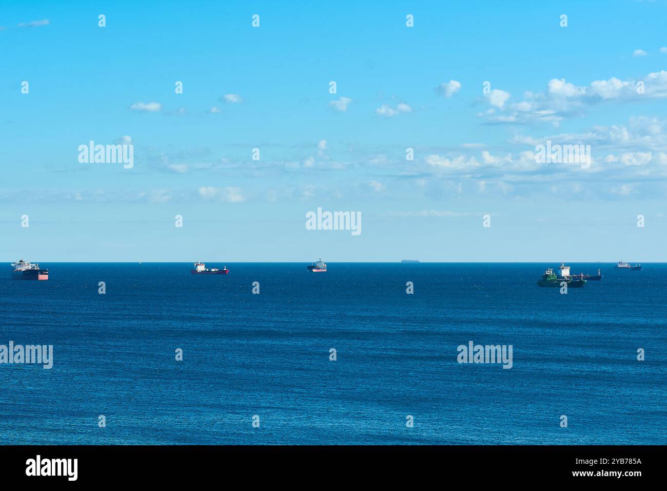 Una tranquilla scena di navi da carico sparse in un vasto mare blu con un cielo limpido sopra la testa. Immagine ideale per i temi dei trasporti, del commercio internazionale, Foto Stock