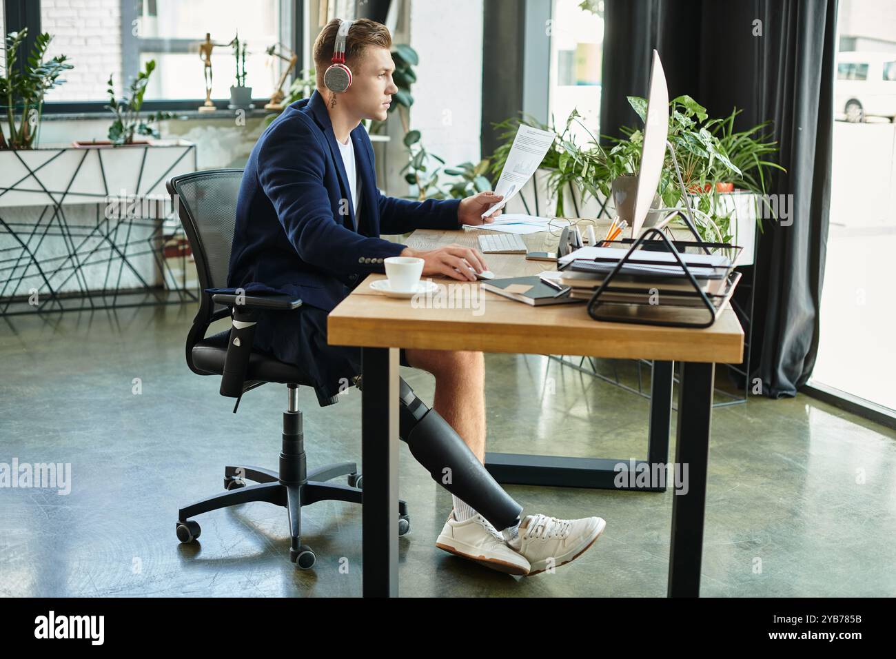 Un giovane con una disabilità lavora diligentemente alla sua scrivania moderna, mostrando determinazione e inclusività. Foto Stock