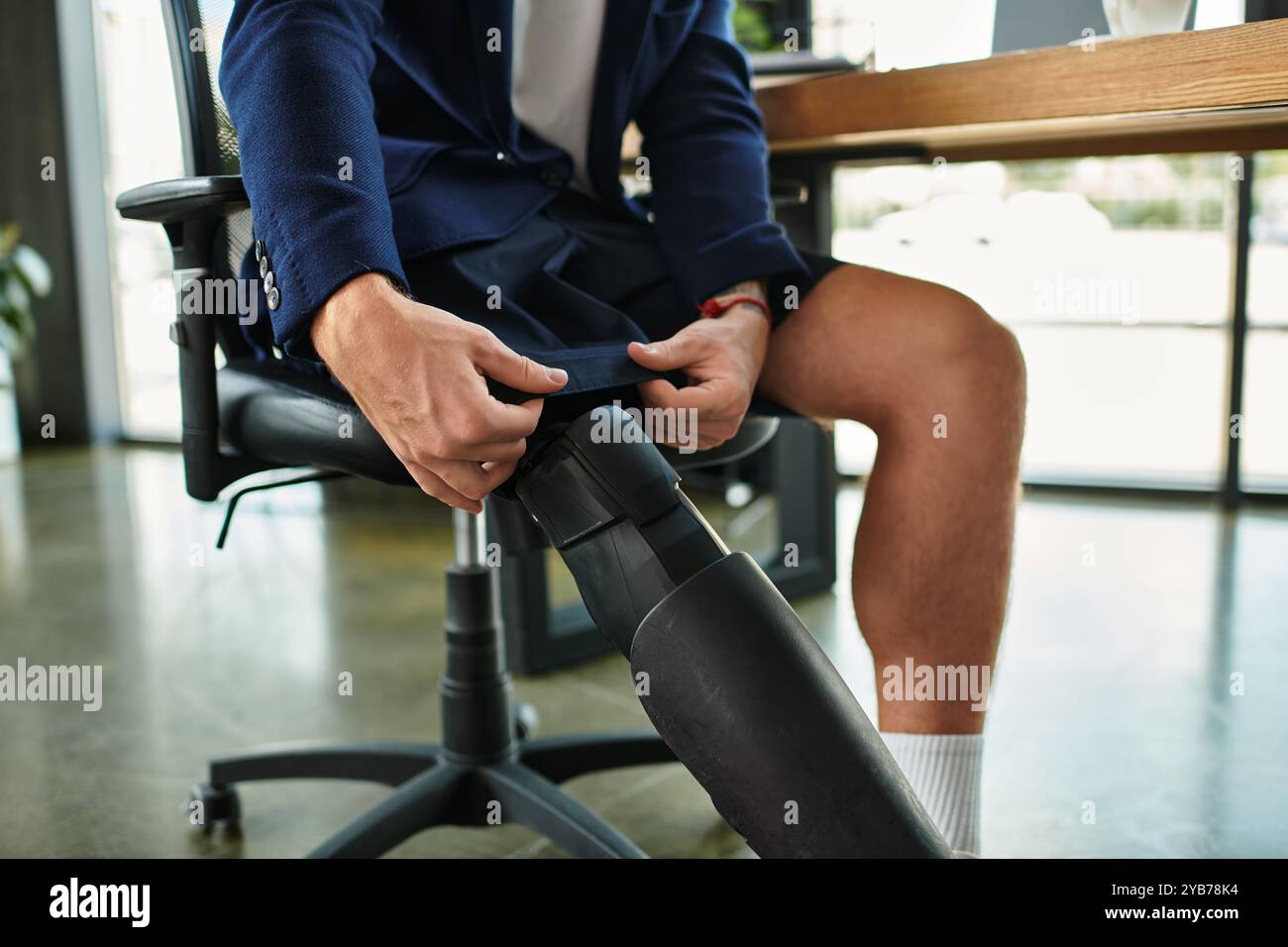 Un giovane e affascinante uomo d'affari con disabilità adatta i suoi vestiti mentre è seduto in un ufficio contemporaneo. Foto Stock