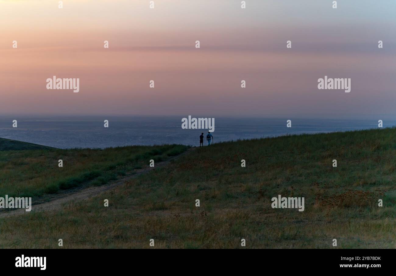 Due persone stanno ai margini della strada e guardano giù la collina al panorama della città notturna. Foto Stock