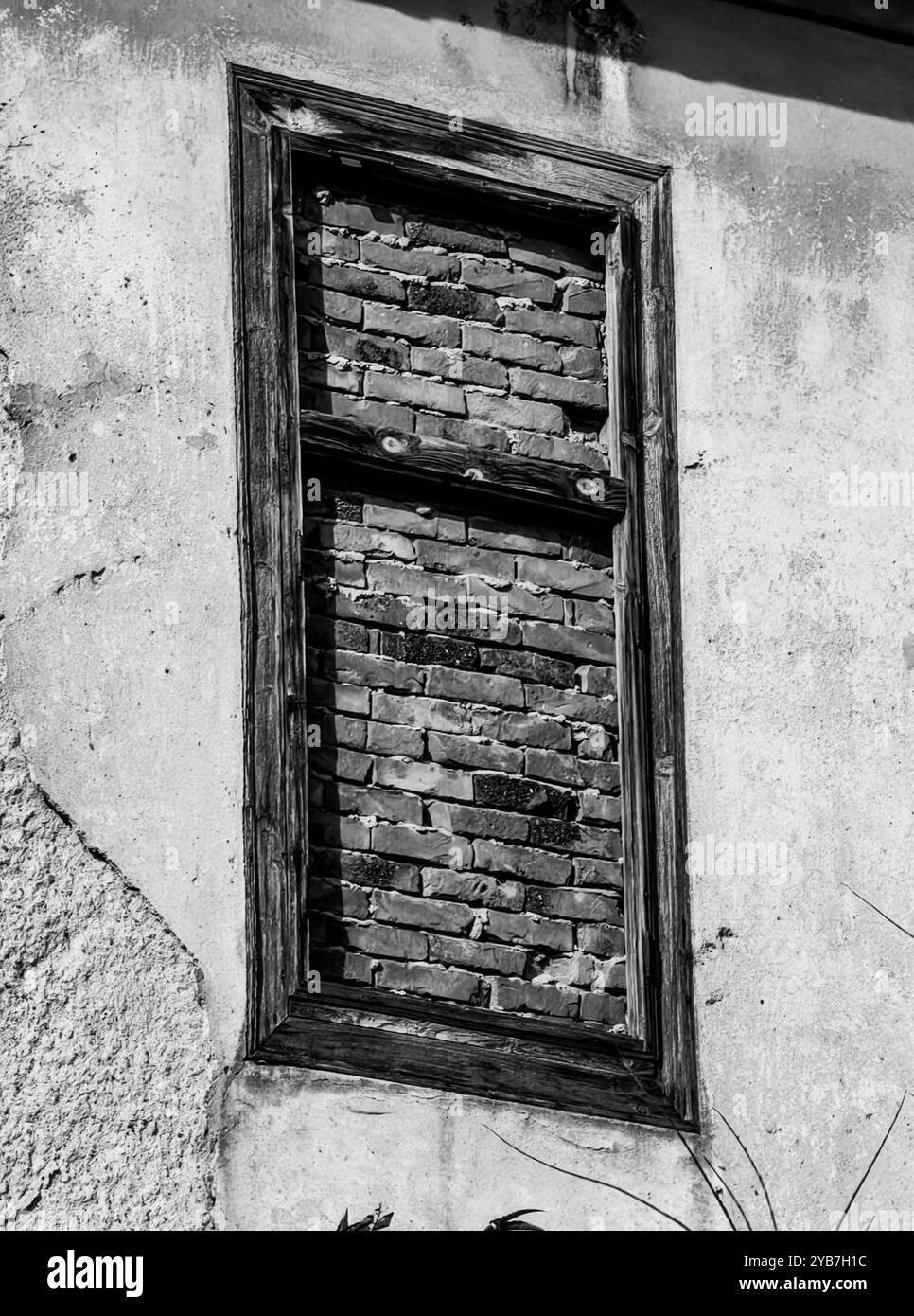 Casa abbandonata: Vecchia finestra in legno con barricate di mattoni. Bianco e nero. Foto Stock