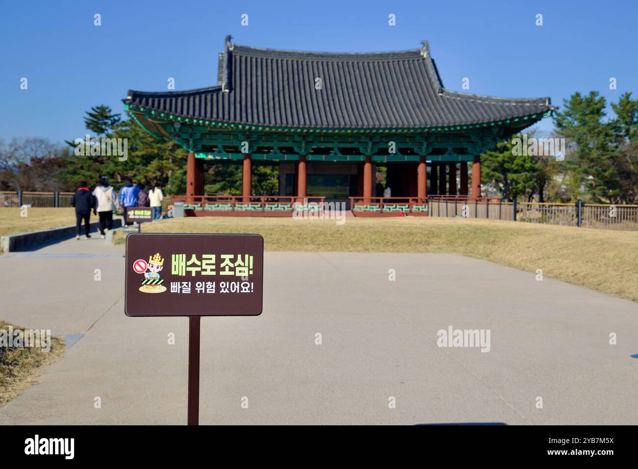 Gyeongju, Corea del Sud - 11 novembre 2023: Un cartello di attenzione che avverte i visitatori circa i pericoli di scivolamento si trova di fronte ad un tradizionale padiglione coreano A. Foto Stock