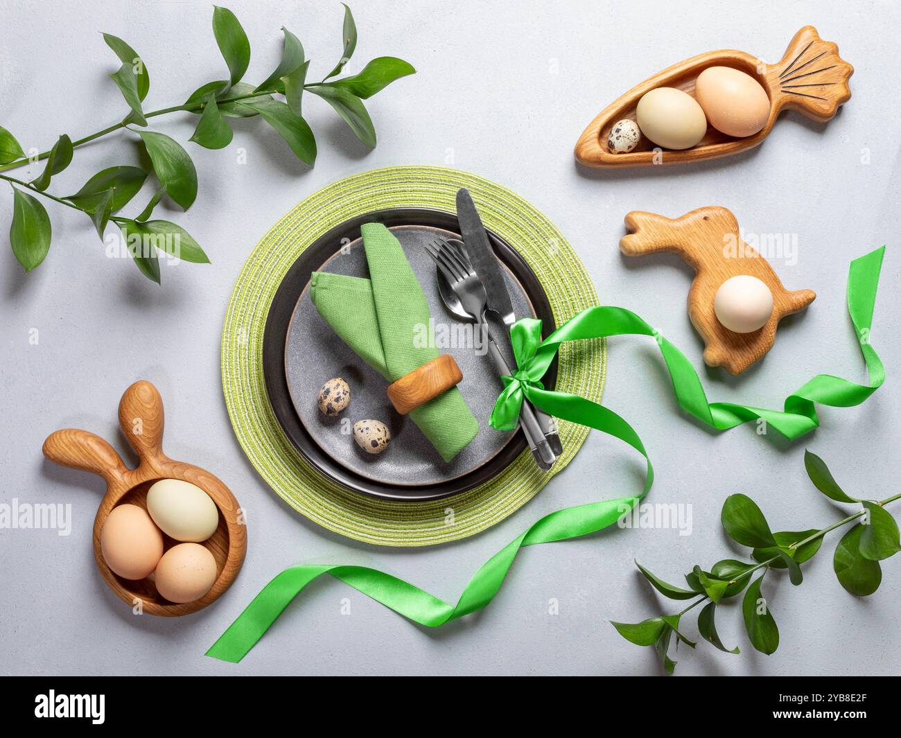 Vista dall'alto alla tavola di Pasqua. Ambiente di vacanza dai colori naturali. Piatti rotondi e figurati, tovaglioli verdi e nastro, uova biologiche, posate, primavera Foto Stock
