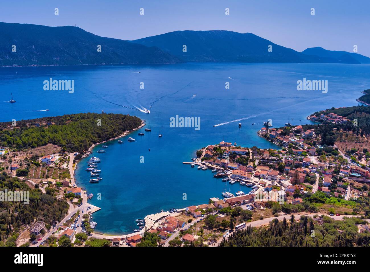 Veduta aerea di Fiskardo, Cefalonia. Pittoresco villaggio adagiato su una penisola, circondato da acque turchesi. Case colorate, piccola spiaggia e barca Foto Stock