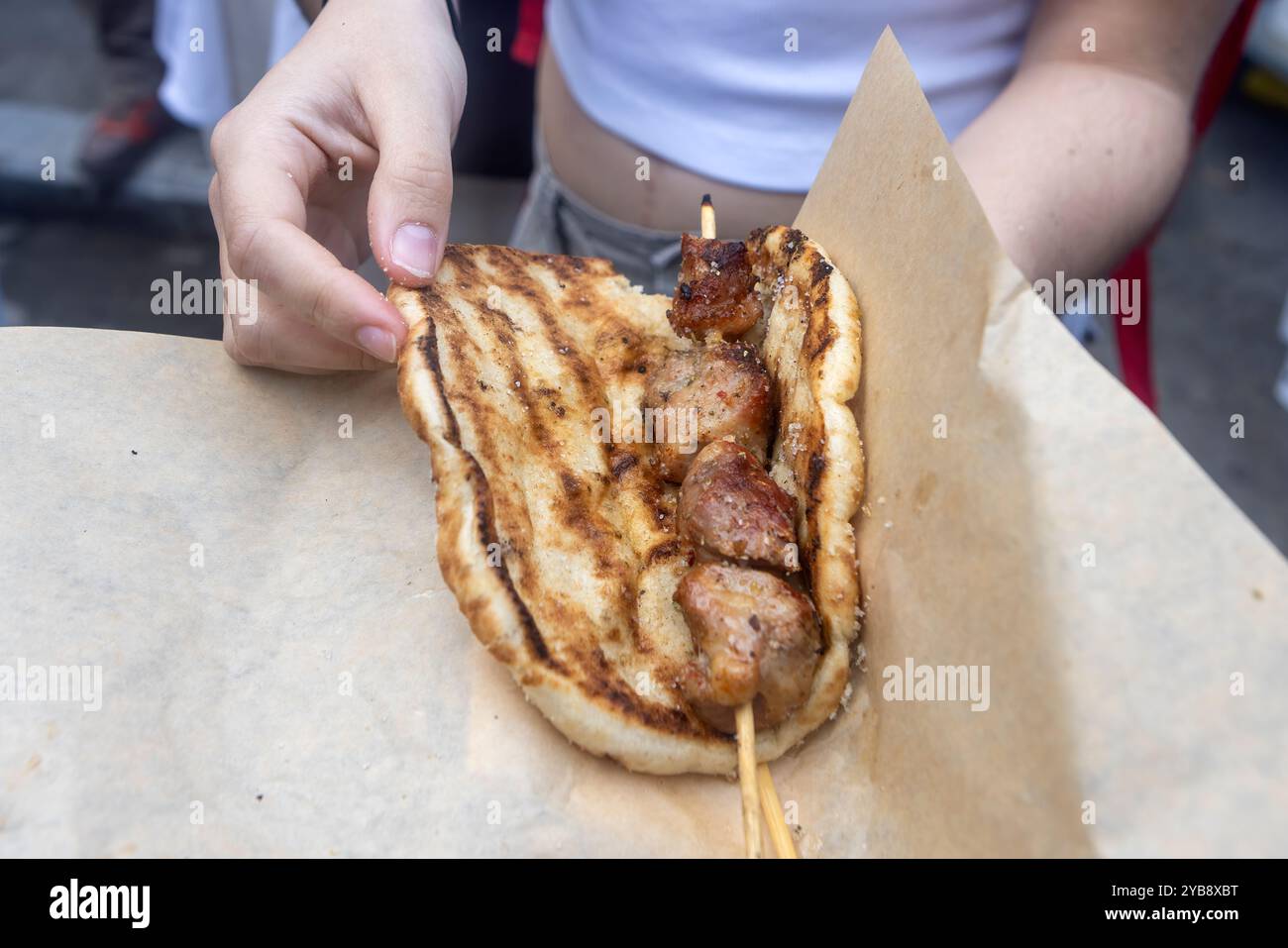 Una persona tiene in mano una pita alla griglia avvolta intorno a uno spiedino di carne alla griglia. Il piatto sembra essere un tradizionale cibo di strada, con la pita carbonizzata Foto Stock