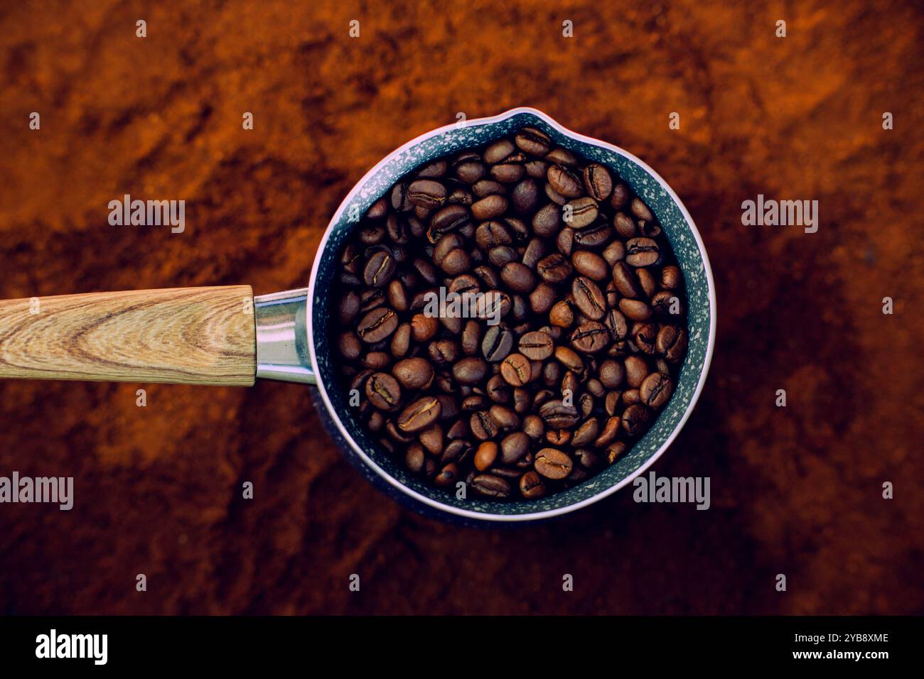 Vista dall'alto di una caffettiera con manico in legno. All'interno, vengono posizionati i chicchi di caffè tostati. La caffettiera si trova sopra il caffè macinato. Foto Stock