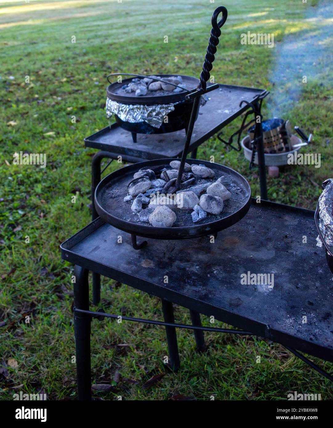 Cucinare all'aperto utilizzando il forno olandese in ghisa e brichette di carbone. Si può immaginare l'aroma del carbone di affumicatura e ci si chiede quale sia il delizioso ingresso Foto Stock