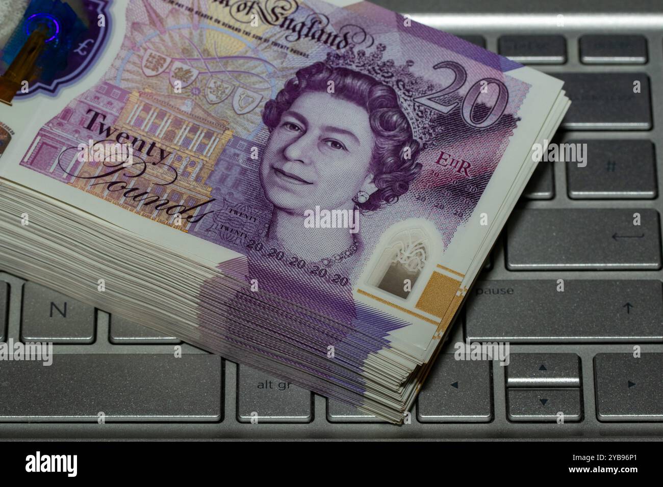 Una pila di banconote da 20 libbre poggia su una tastiera argentata per laptop, con la nota superiore che mostra l'immagine della regina Elisabetta II Foto Stock