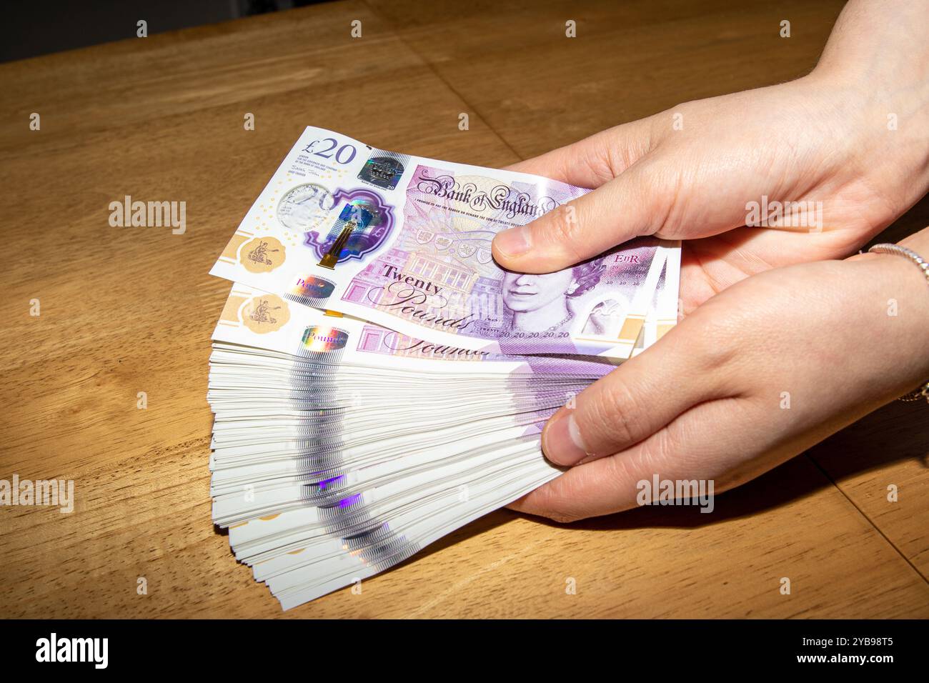 Una persona in possesso di un fan di banconote da 20 sterline in un ambiente informale. Le banconote sono colorate e presentano figure di spicco, che mostrano la valuta Foto Stock