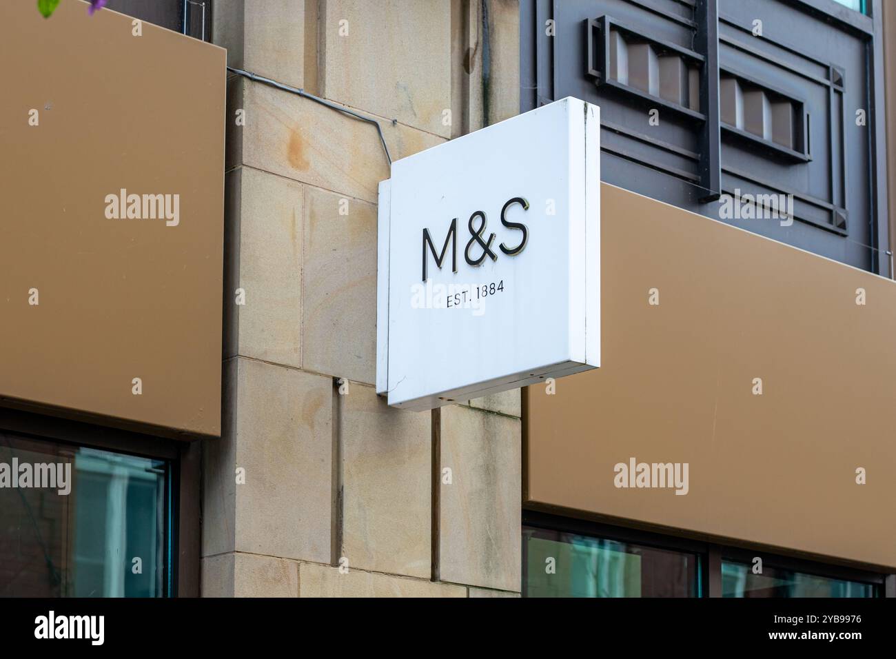 Primo piano di un cartello di un moderno punto vendita con le lettere "M&S" e il testo "EST. 1884 ». Il cartello è montato su un muro di pietra, che mostra una truffa Foto Stock