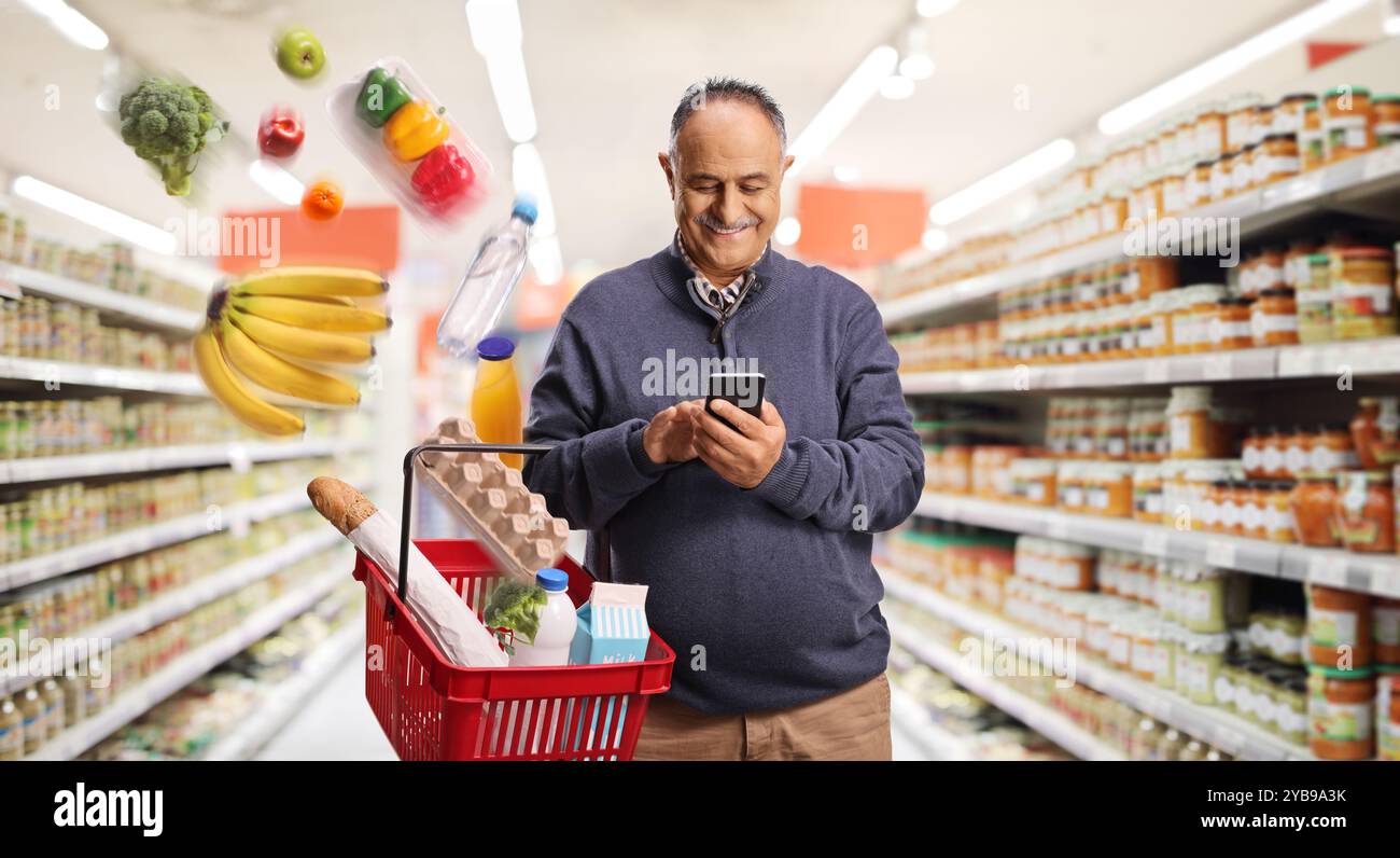 Uomo maturo felice che ordina generi alimentari online e prodotti che cadono in un cestino in un supermercato Foto Stock