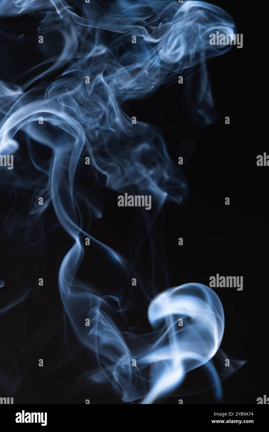 L'immagine presenta morbidi tendini arricciati di fumo che si innalzano graziosamente su uno sfondo nero profondo, evocando un'aria di mistero e calma. Foto Stock