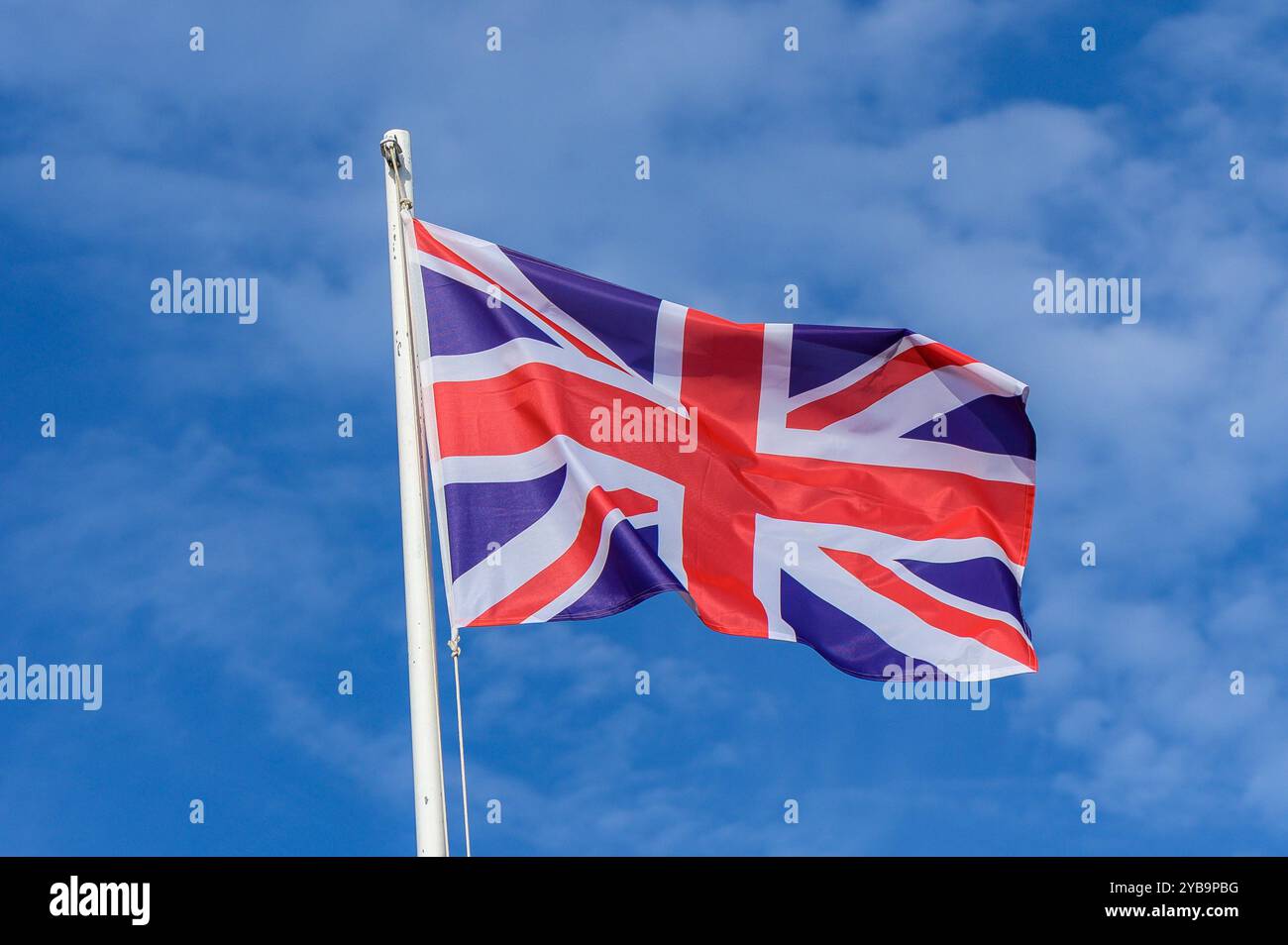 Una forte raffica di vento cattura l'Union Jack mentre ondeggia con grazia contro un cielo azzurro limpido, simboleggiando l'unità e l'orgoglio della cultura britannica in un bri Foto Stock