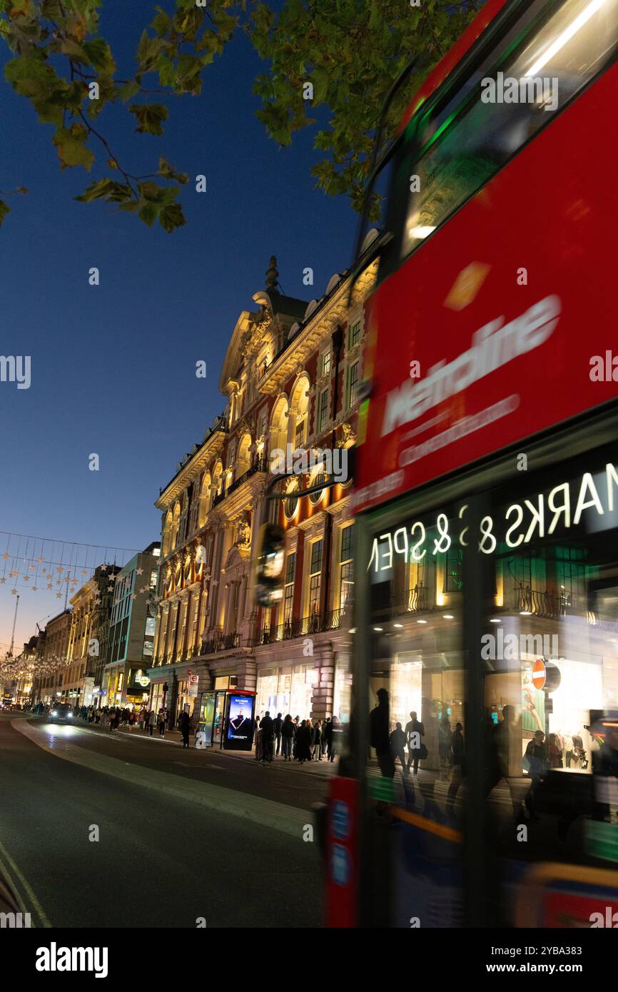Vista notturna di Oxford Street, Londra. I pedoni e un autobus rosso di Londra passano accanto agli iconici edifici illuminati. Foto Stock