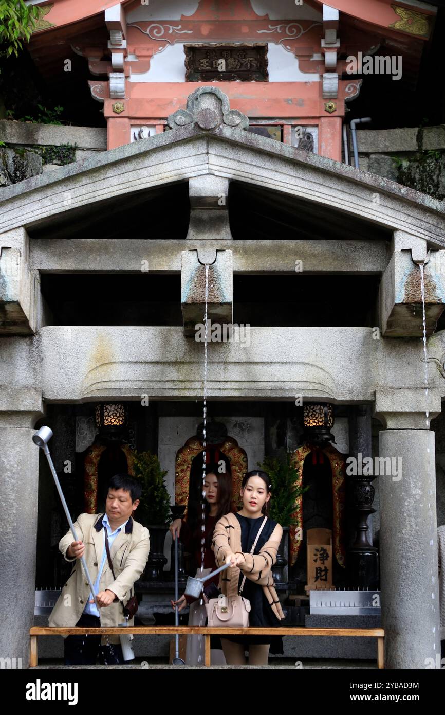 Un gruppo di visitatori utilizza tazze con manico lungo per raccogliere l'acqua dai torrenti della cascata di Otowa e bere nel tempio kiyomizu-dera. Le persone credono che bere l'acqua di questo torrente porterà amore, successo e longevità alla loro vita. Kyoto, Giappone Foto Stock