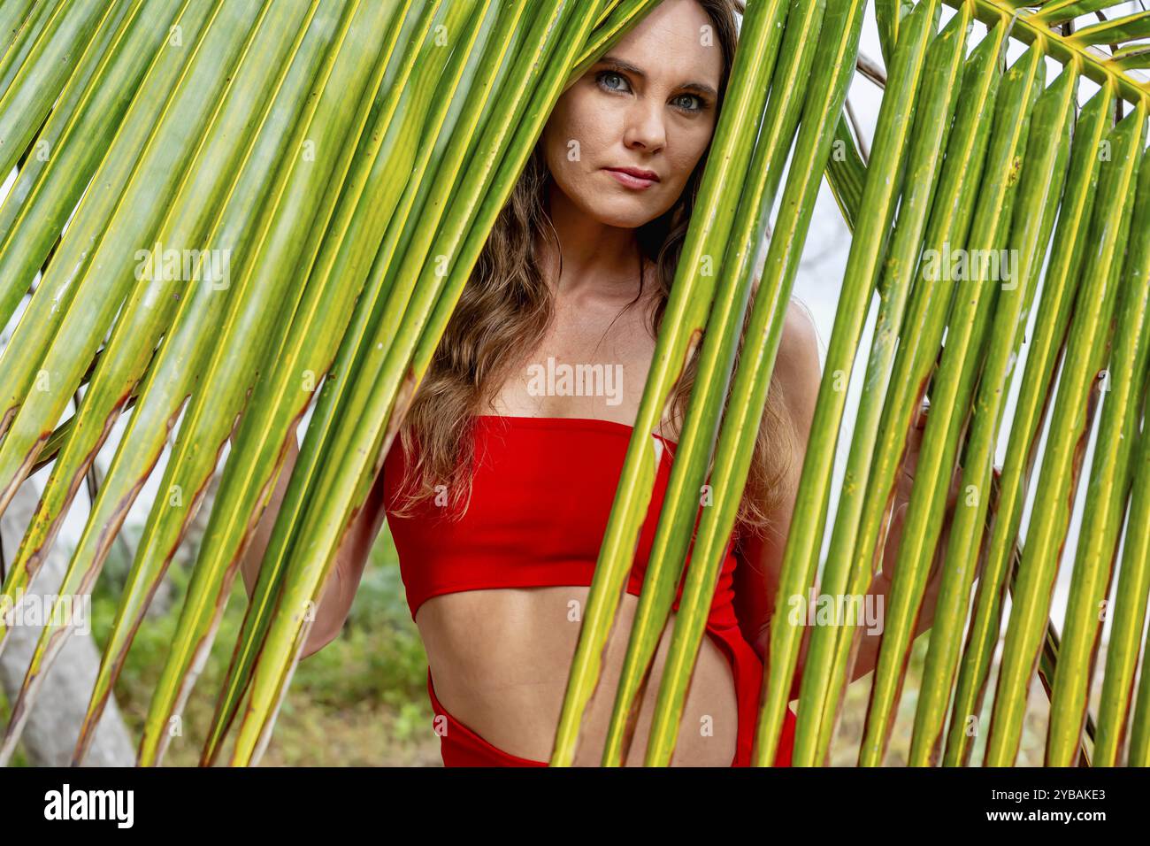 La splendida bruna, splendente in un vivace abito rosso, abbellisce le coste caraibiche con eleganza, incarnando la bellezza nel paradiso tropicale Foto Stock