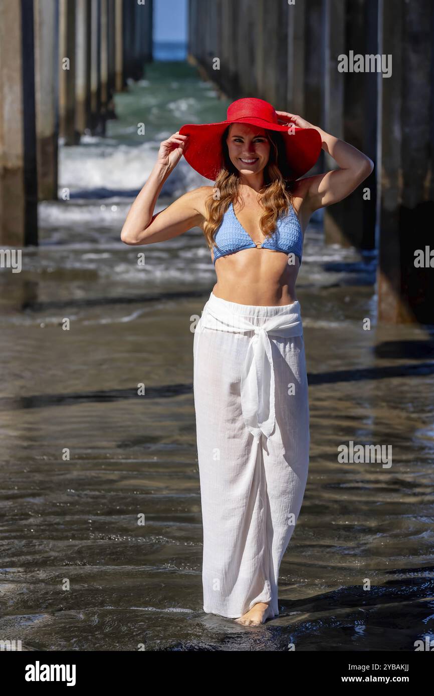 Una donna mozzafiato si crogiola nella beatitudine della spiaggia, vicino a un molo, sotto cieli azzurri, abbracciando la serenità di una giornata perfetta in riva al mare Foto Stock