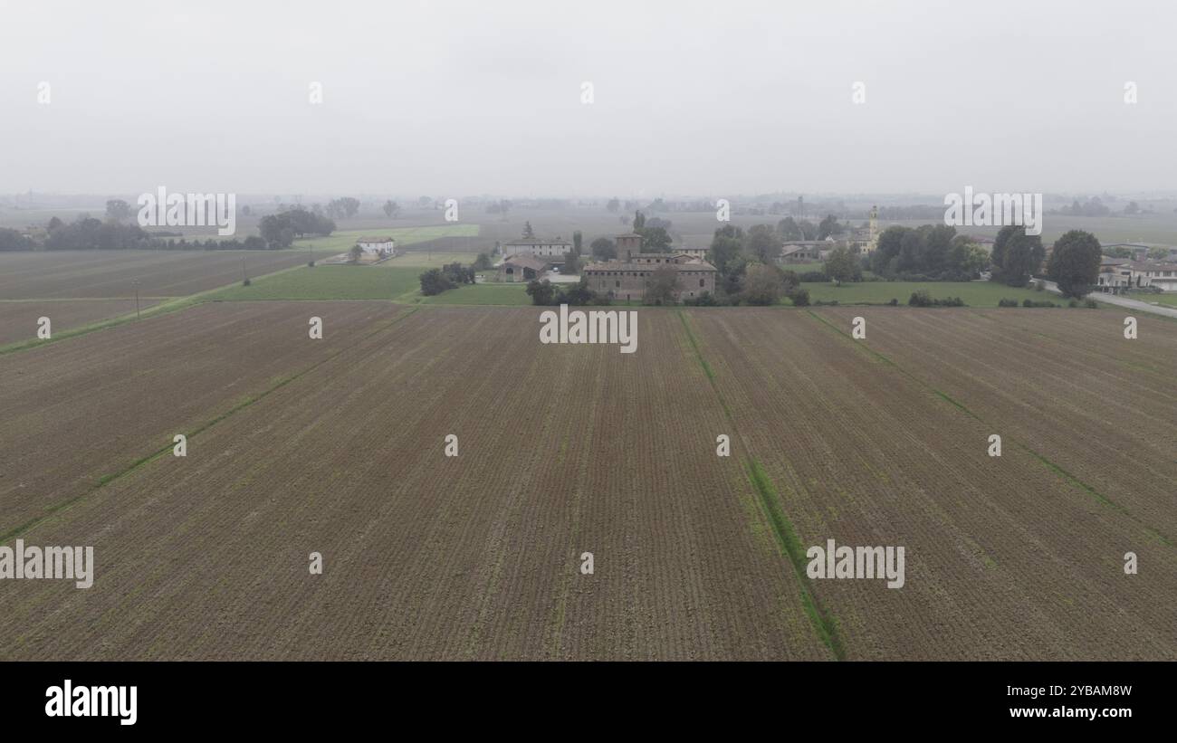 Un grande campo vuoto con un edificio lontano sotto un cielo coperto nella campagna di Muradello, PC Italia Foto Stock