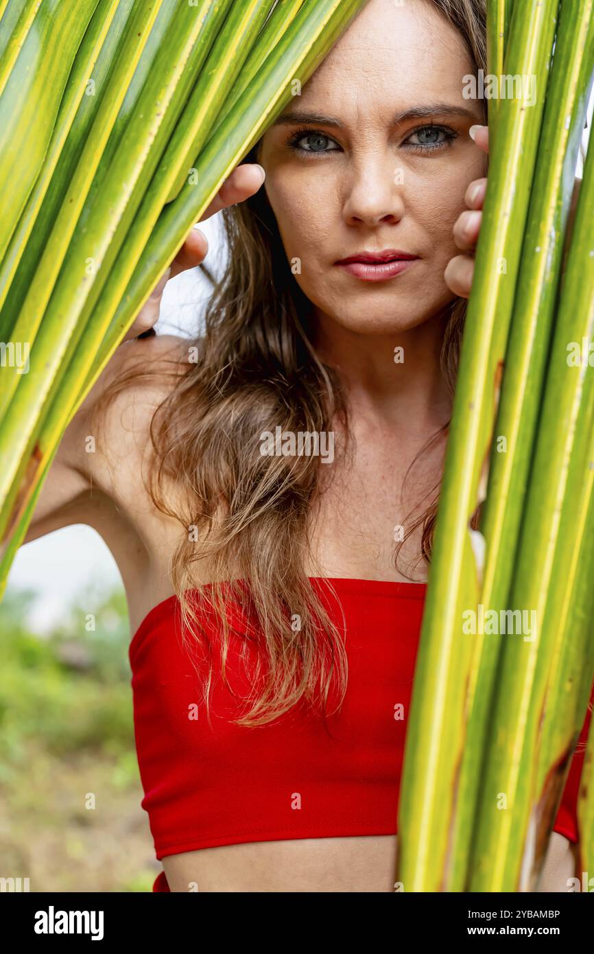 La splendida bruna, splendente in un vivace abito rosso, abbellisce le coste caraibiche con eleganza, incarnando la bellezza nel paradiso tropicale Foto Stock