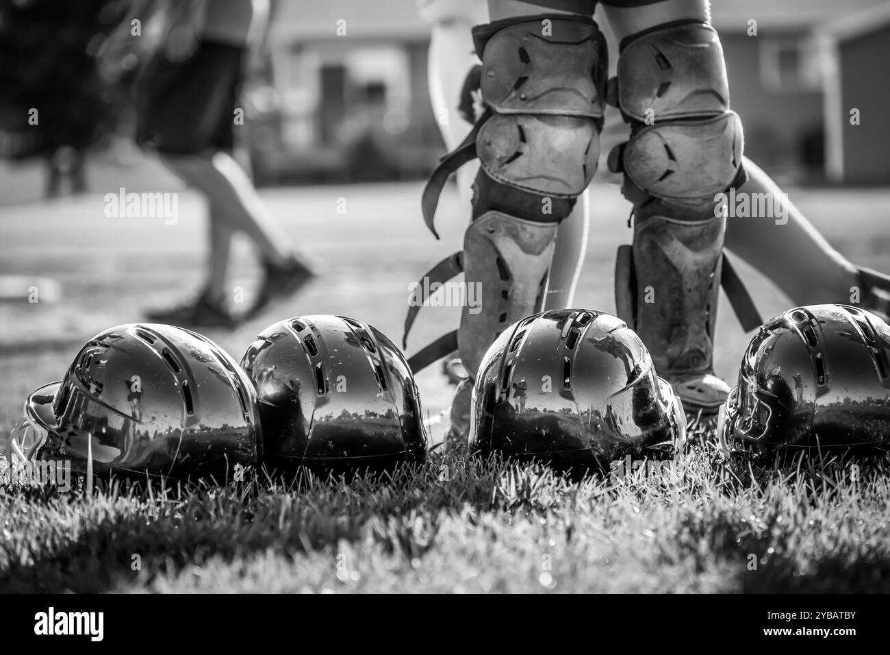 Fila di caschi da baseball giovani nell'erba con un campo deconcentrato sullo sfondo. Foto Stock
