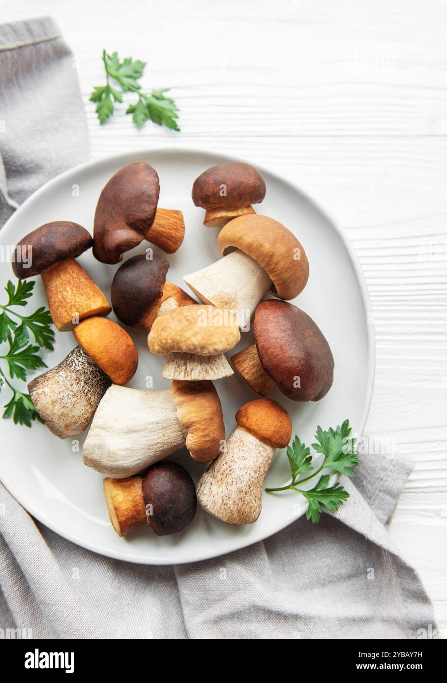 Un assortimento di funghi freschi è disposto su un piatto, mostrando forme e colori diversi, accompagnati da prezzemolo su un backgroun di legno testurizzato Foto Stock