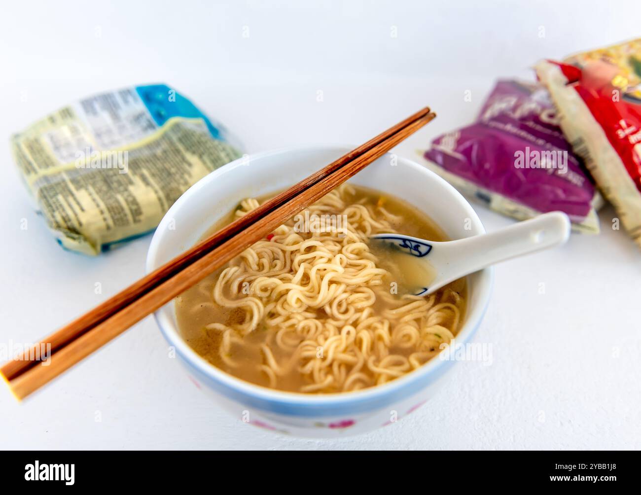 Una ciotola di spaghetti istantanei a base di zuppa con un paio di bacchette e cucchiaio di ceramica e confezioni di spaghetti isolati su bianco. Foto Stock