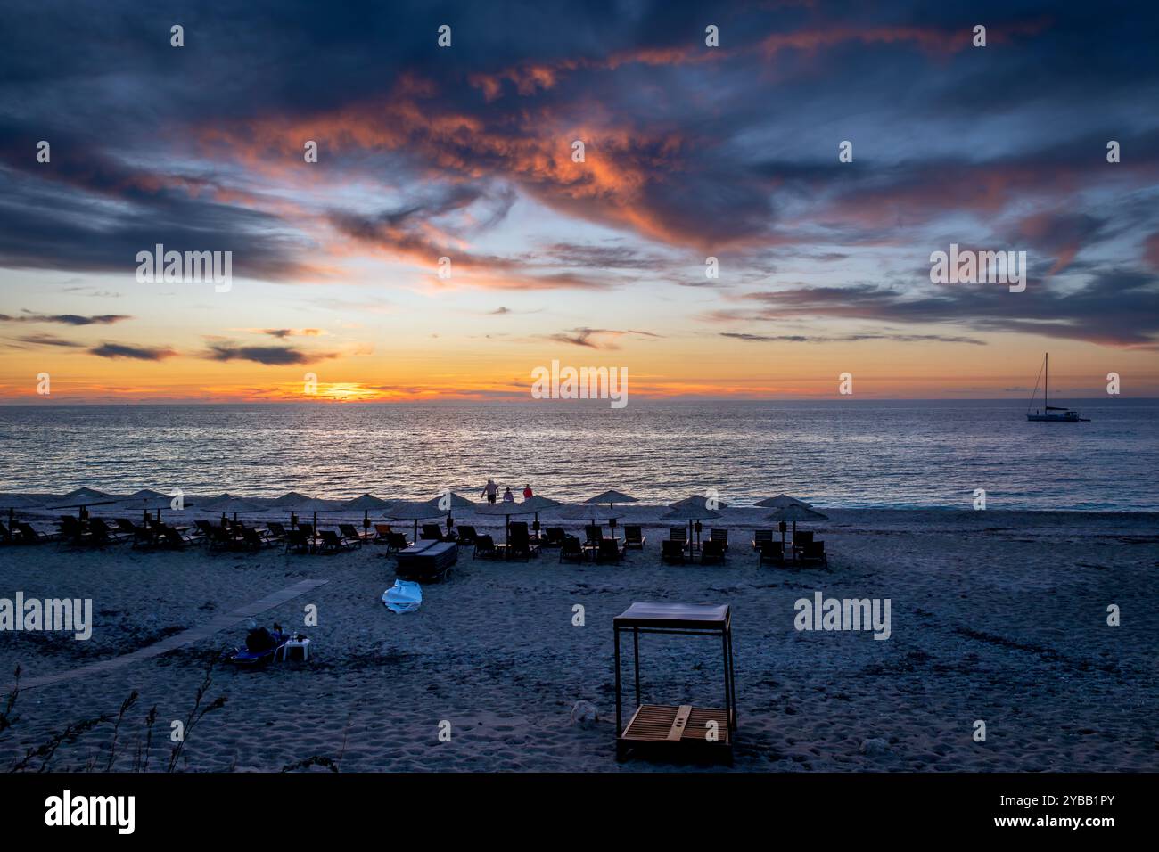 Kathisma Beach, isola di Lefkada, Grecia, con lettini, ombrelloni, e i turisti che si godono gli splendidi ultimi raggi del sole mentre il sole tramonta sotto il mare horizo Foto Stock