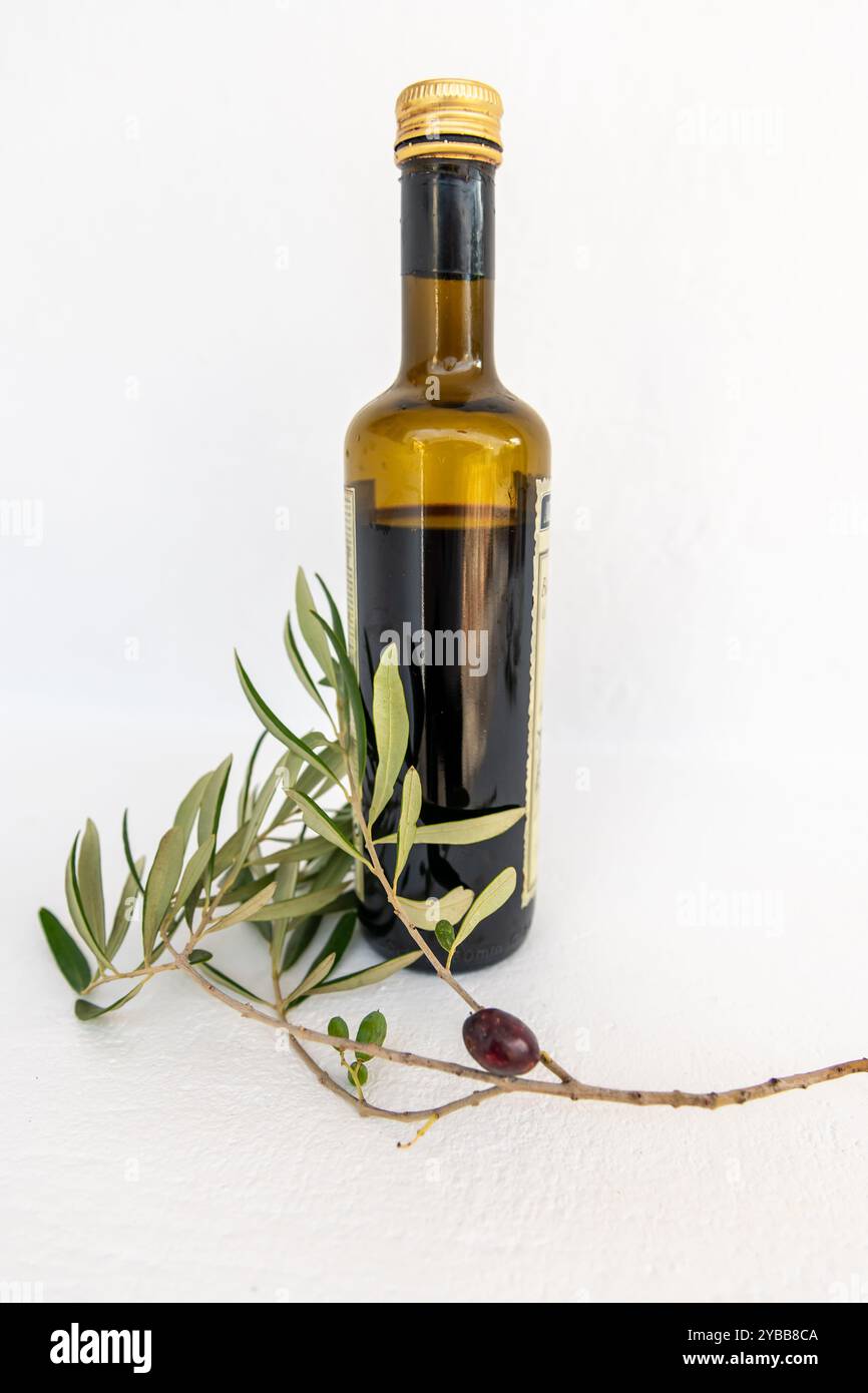 Vista laterale di una bottiglia di olio d'oliva con oliva nera su un ramo, isolata su sfondo bianco, Foto Stock