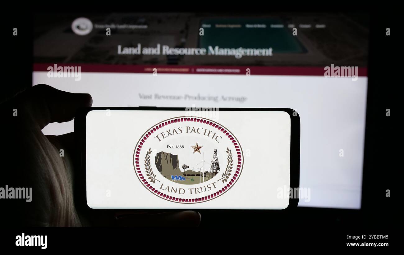 Persona che possiede uno smartphone con il logo della società statunitense Texas Pacific Land Corporation sullo schermo davanti al sito Web. Mettere a fuoco il display del telefono. Foto Stock