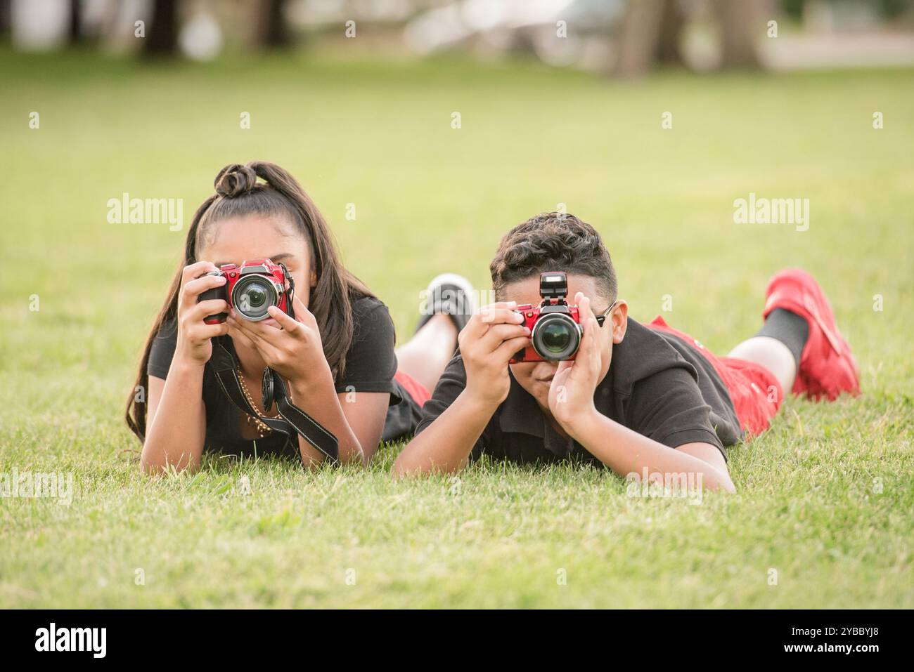 Ragazzo e ragazza stesi nell'erba a scattare foto con le loro macchine fotografiche Foto Stock