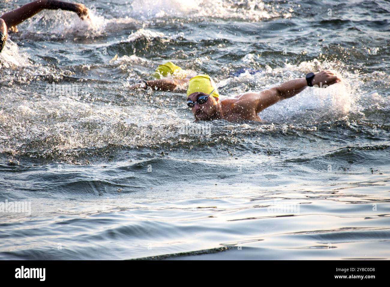 Triatleta che nuota in mare aperto, indossando un berretto giallo Foto Stock