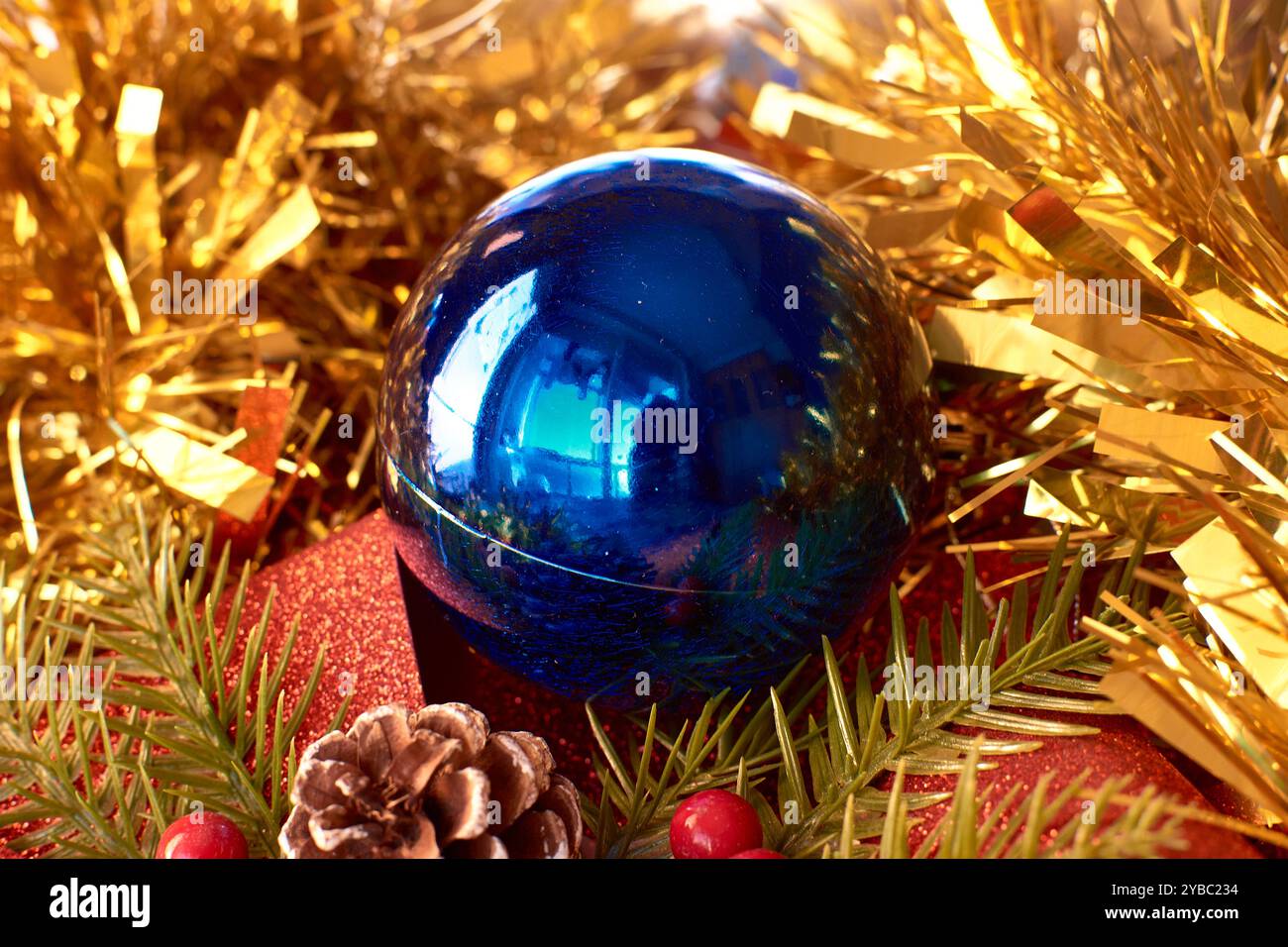 Una decorazione natalizia colorata e festosa, caratterizzata da un bauble blu luminoso circondato da un fiocco rosso scintillante, pineconi e rami sempreverdi con Foto Stock