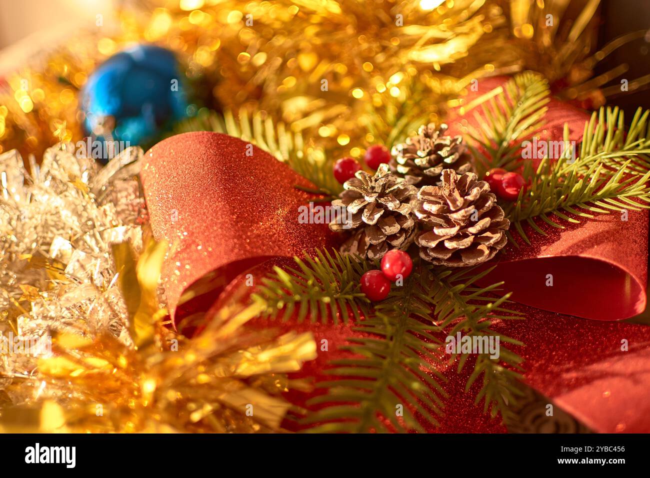 Una decorazione natalizia colorata e festosa, caratterizzata da un bauble blu luminoso circondato da un fiocco rosso scintillante, pineconi e rami sempreverdi con Foto Stock