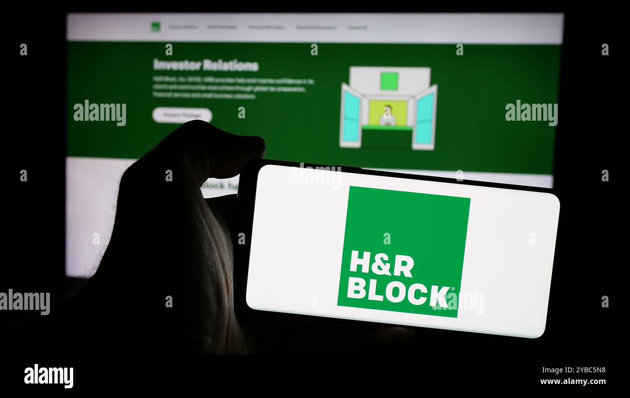 Persona che detiene uno smartphone con il logo della società statunitense di preparazione fiscale HR Block Inc. Sullo schermo davanti al sito Web. Mettere a fuoco il display del telefono. Foto Stock