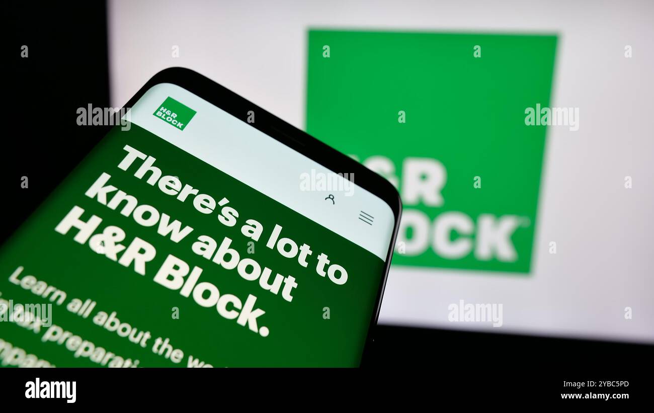 Telefono cellulare con sito Web della società di preparazione fiscale statunitense HR Block Inc. Sullo schermo di fronte al logo aziendale. Mettere a fuoco in alto a sinistra sul display del telefono. Foto Stock