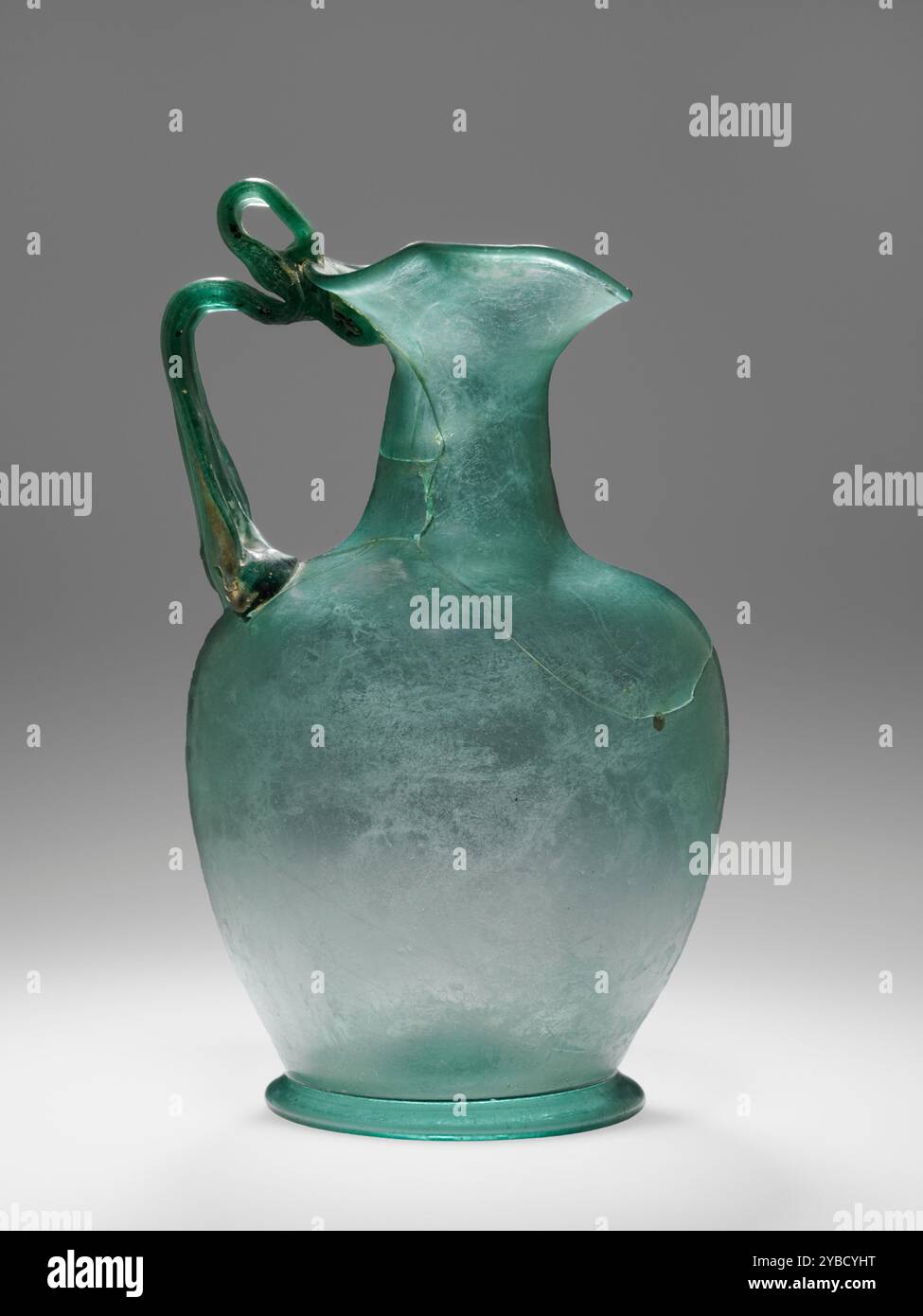 Oinochoe, III secolo d.C. ulteriori informazioni: Oinochoe soffiato libero di vetro blu-verde traslucido. Il grande recipiente ha un piede poco profondo e una spessa impugnatura a nastro che collega la spalla al bordo del traliccio. L'impugnatura è piegata vicino al bordo per creare una presa per le dita. Il vaso è intatto, ma presenta diverse interruzioni visibili. Si è verificato solo un lieve deterioramento. Foto Stock
