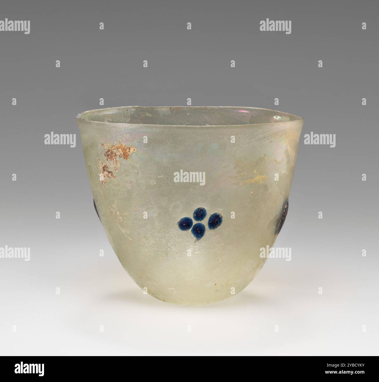 Becher o lampada, IV-V secolo d.C. informazioni aggiuntive: Vaso in vetro verde pallido. Il vaso ha una forma conica con una bocca larga. E' scarsamente decorata con piccoli lobi di vetro blu: Sui lati opposti si trova una coppia di grandi lobi; sugli altri lati opposti si trova una coppia di quattro piccoli lobi disposti a croce. C'è un certo scolorimento dovuto agli agenti atmosferici e a una leggera iridescenza. Foto Stock