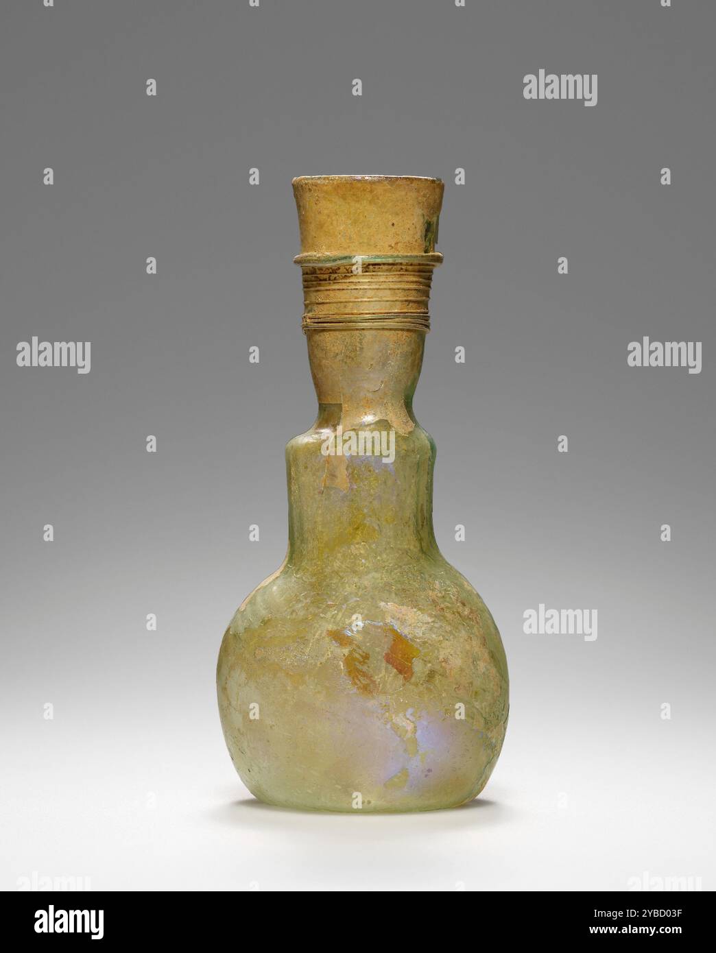 Fiasca, IV-V secolo d.C. ulteriori informazioni: Questa fiasca soffiata è realizzata in vetro verde chiaro. Il suo corpo simile a una lampadina poggia su una base concava. Il collo svasato, leggermente stretto alla sua base, è ornato da decorazioni trainate. Questa fiasca è in buone condizioni. La sua superficie presenta una leggera lucentezza iridescente sul corpo e un po' di scaglie sul collo. Foto Stock
