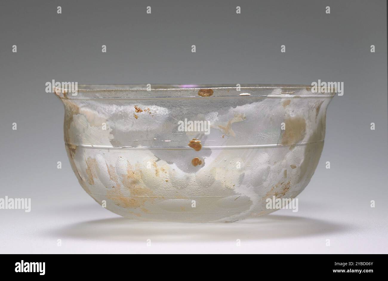 Ciotola, II-III secolo d.C. ulteriori informazioni: Questa piccola ciotola è realizzata in vetro incolore. Il suo corpo emisferico con base piatta è stato lucidato e decorato con linee e scanalature tagliate sul tornio. Il bordo svasato è stato rotto e lucidato. Questa ciotola è in buone condizioni. La superficie presenta una leggera lucentezza iridescente e qualche sfaldamento. Sono stati aggiunti piccoli riempimenti sulla base. Foto Stock