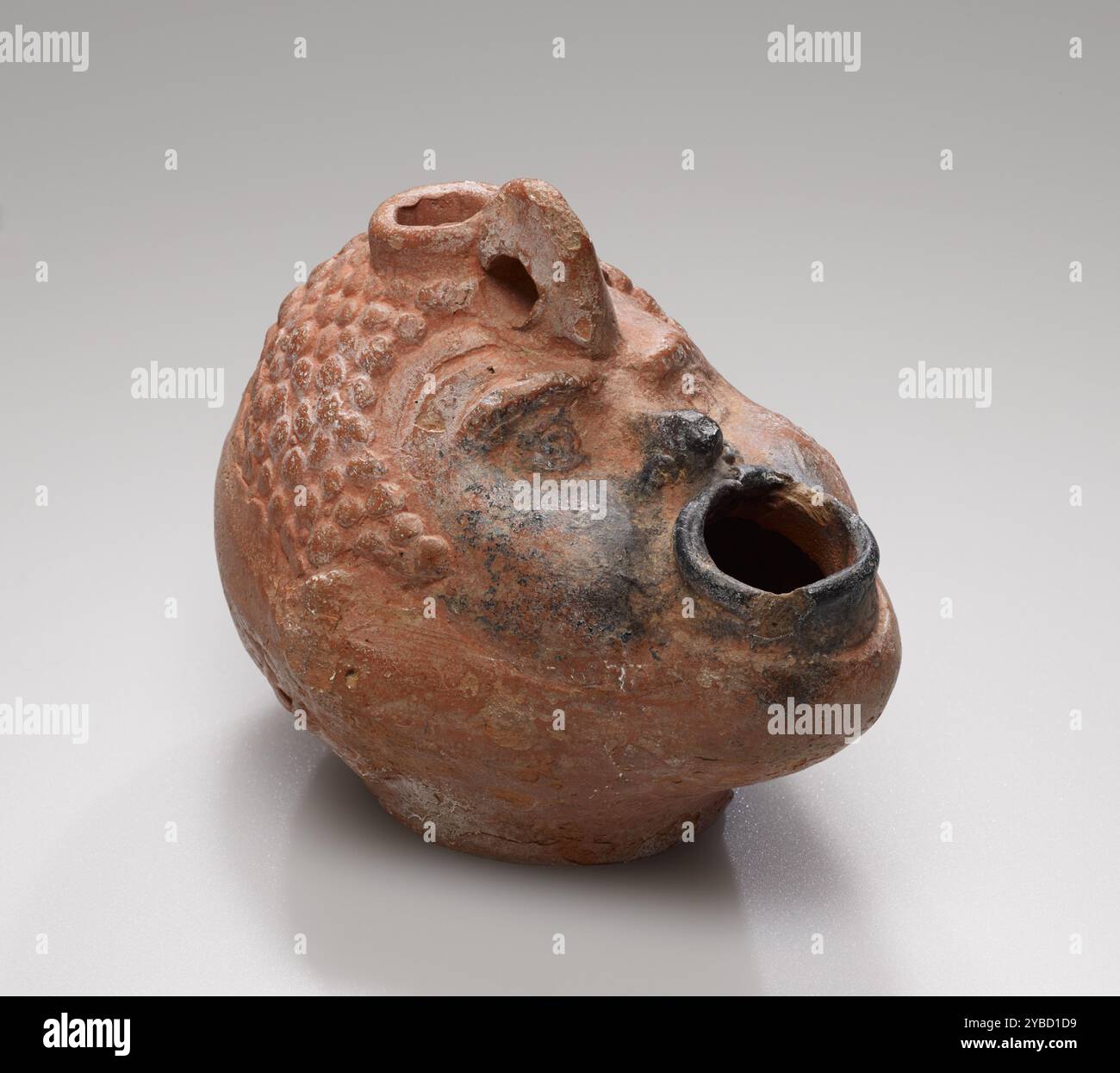 Lamp, 1st Century a.C.-4th Century d.C. ulteriori informazioni: Questa lampada globulare a forma di maschio nero africano’s testa è stata realizzata con uno stampo. Le file strette di punti concentrici impressi indicano capelli ricci e gli occhi della figura’si guardano molto. Ha un naso lieve e appuntito, le guance gonfiate e la bocca aperta, che funge da stoppino, danno l'impressione che stia soffiando una fiamma. Tracce chiare di utilizzo sono visibili dai residui di ustioni intorno alla bocca e sul lato destro della lampada’S. Foto Stock