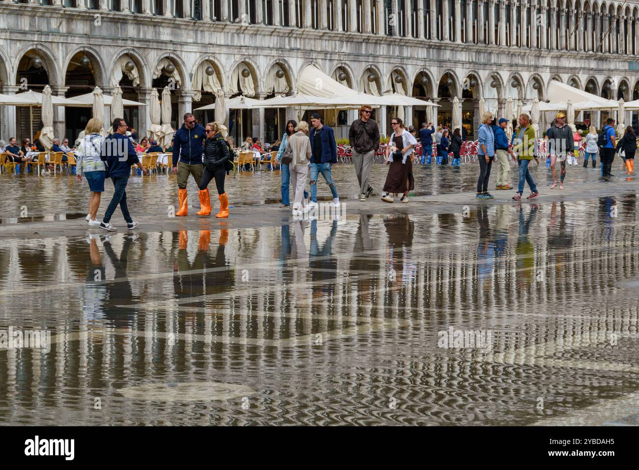 Piazza San Marco allagata a Venezia dopo un'alta marea. I turisti hanno indossato stivali impermeabili in colori brillanti. Foto Stock