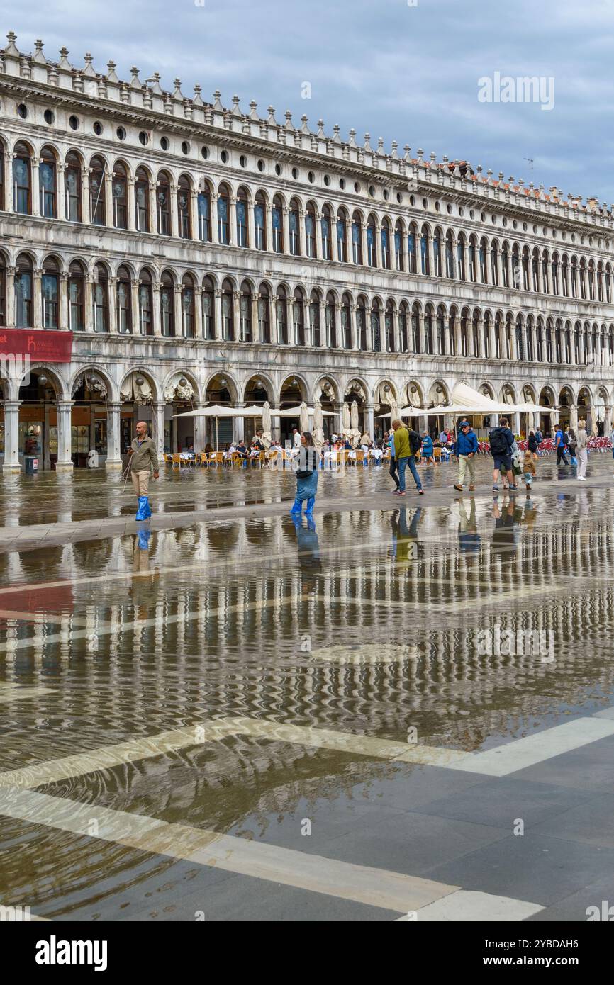 Piazza San Marco allagata a Venezia dopo un'alta marea. I turisti hanno indossato stivali impermeabili in colori brillanti. Foto Stock