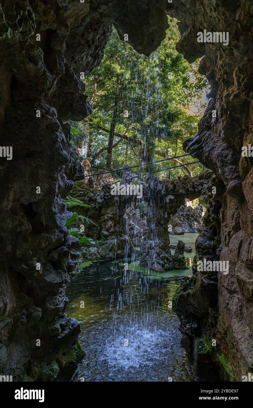 Una tranquilla cascata scorre sopra le rocce circondata da vegetazione lussureggiante e acqua tranquilla. Foto Stock