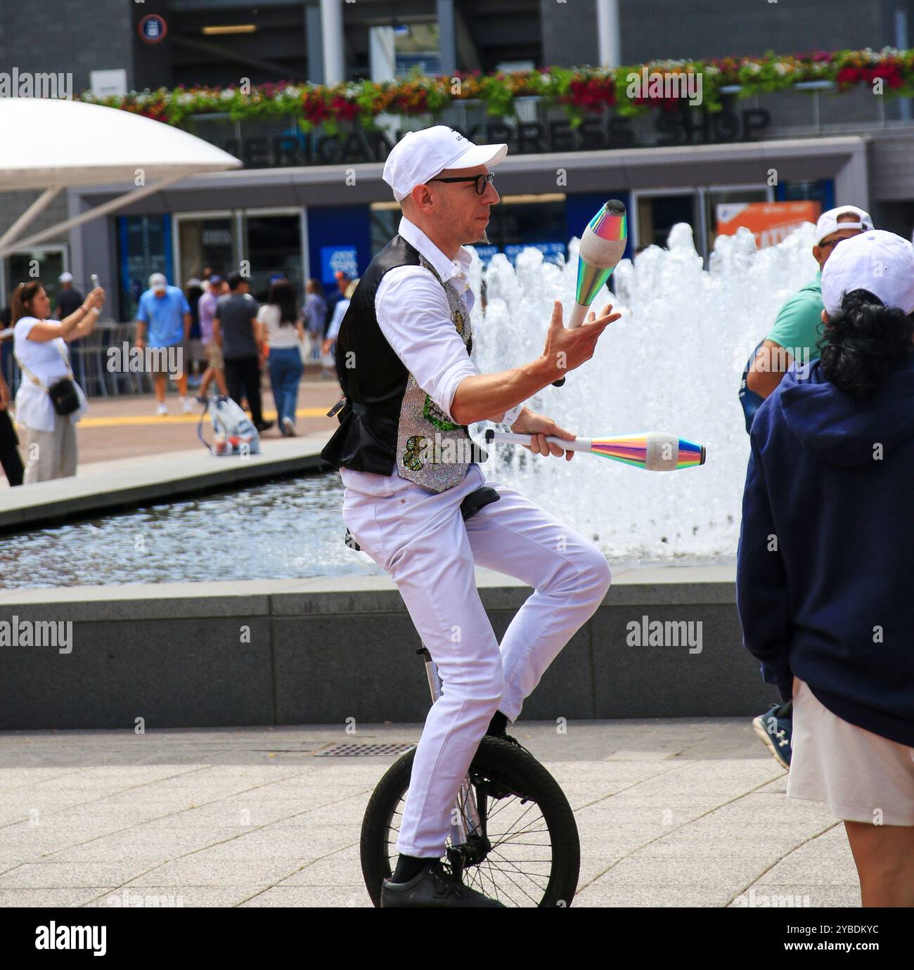 Queens, New York, USA - 20 agosto 2024: Un unicyclist giocherà sapientemente con i club colorati per un pubblico impegnato vicino a una fontana. Foto Stock