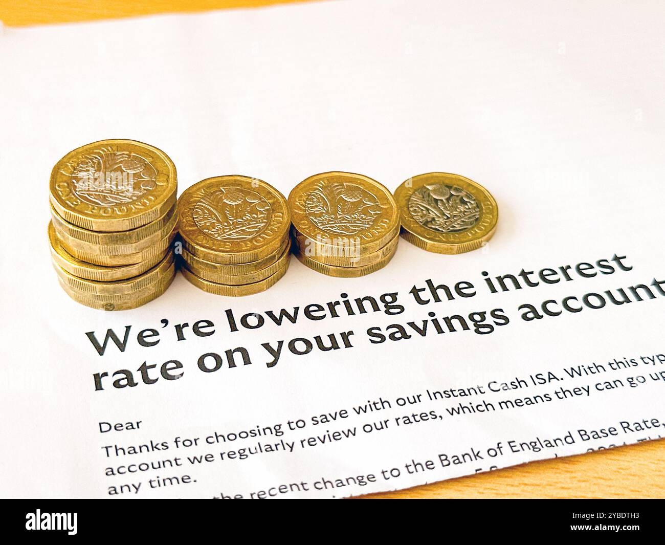 Lettera di una banca anonima che dice a un cliente che i suoi tassi di interesse stanno diminuendo, con colonne di monete da una sterlina di altezza discendente. Niente persone. Foto Stock