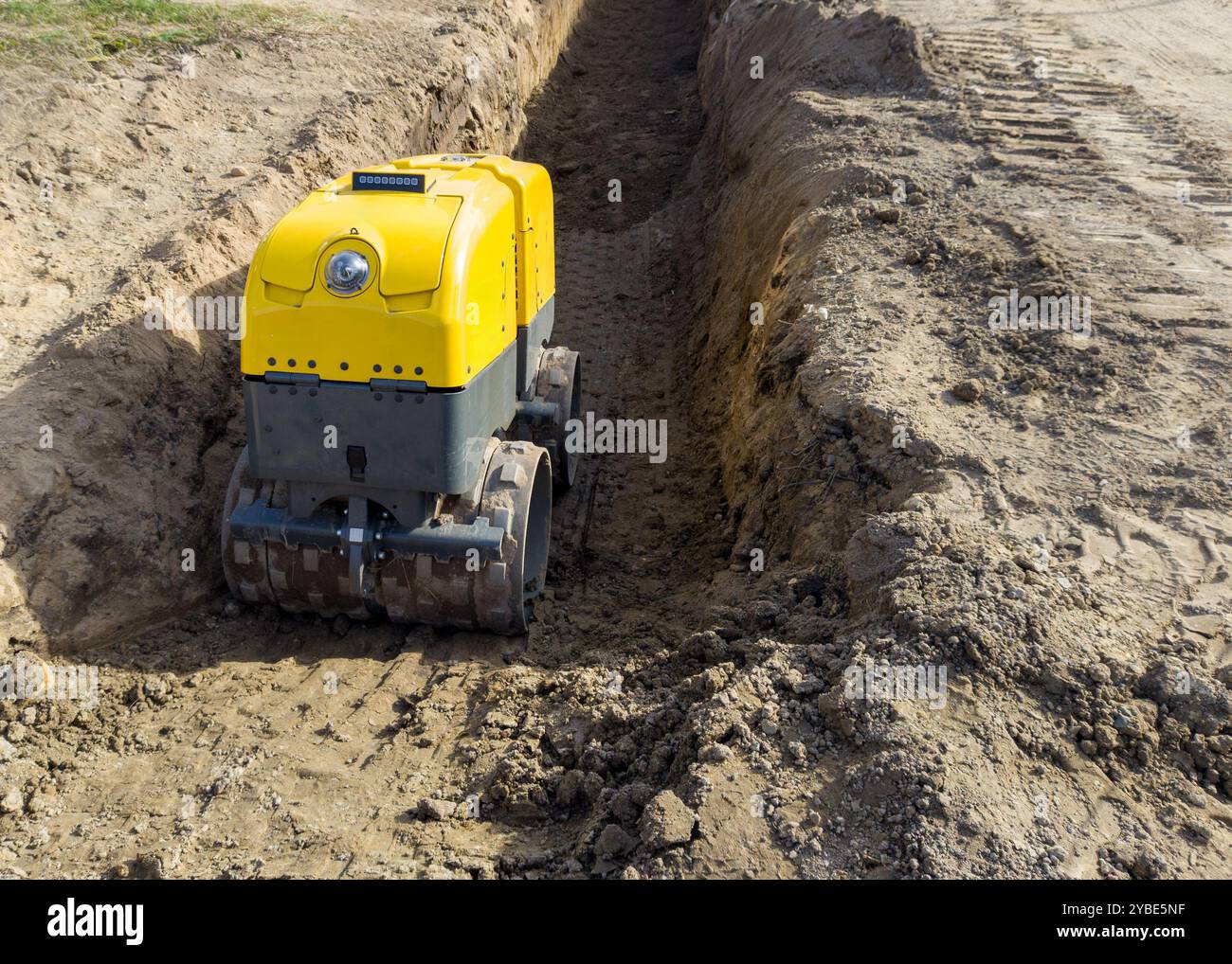 Compattatore per scavi giallo che lavora in scavi stretti in cantiere Foto Stock