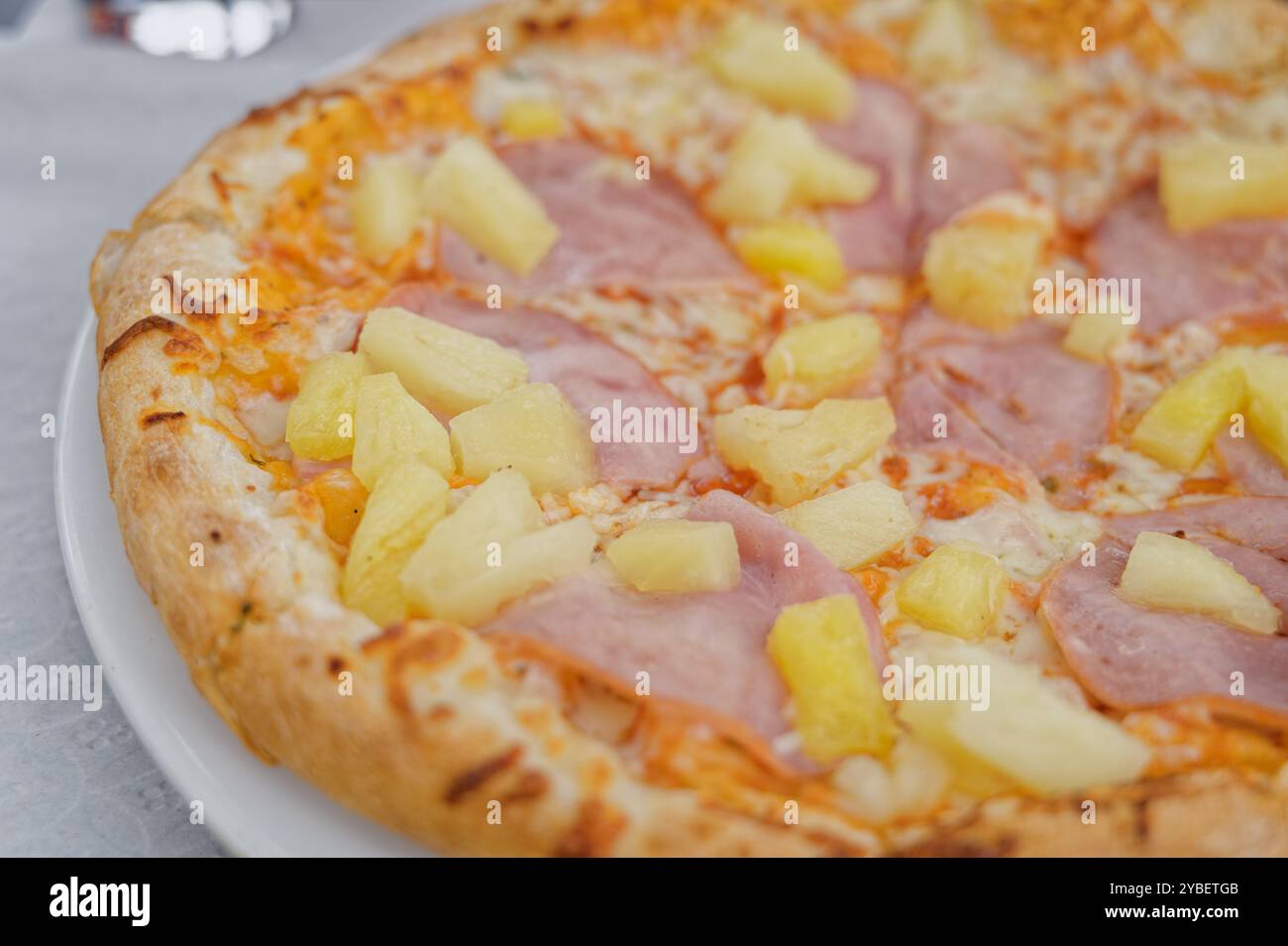 Primo piano di una classica pizza hawaiana condita con prosciutto e succosi pezzi di ananas Foto Stock