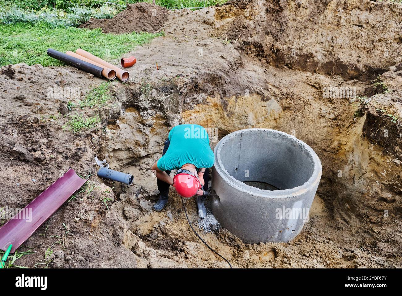 Utilizzando un martello perforatore con scalpello, l'operatore esegue un foro per il tubo fognario nell'anello settico del serbatoio in calcestruzzo. Foto Stock